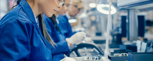 Female electronics factory workers in protective glasses assembling printed circuit boards 