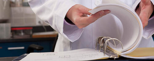 A close up of a lab worker’s hand flipping through three-ring lab binder
