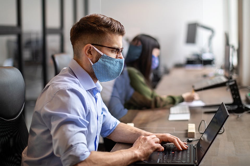 Man working on a laptop while wearing a cloth mask