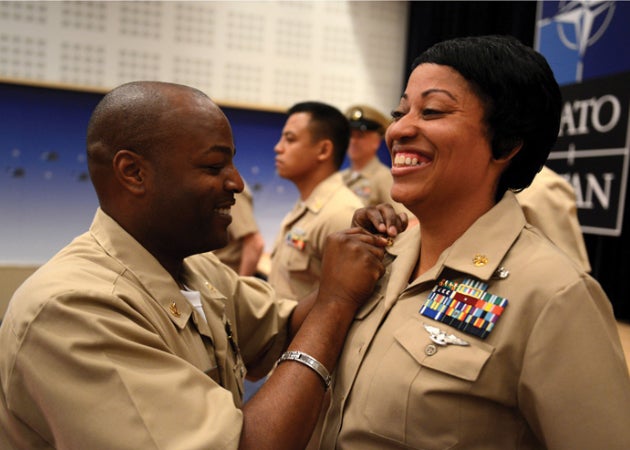 An African American male soldier pins a medal on an African American female soldier while she smiles proudly